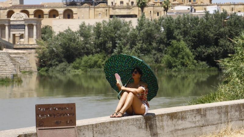 11/07/2022-Una turista se protege del calor con un paraguas y un abanico a la orilla del río Guadalquivir cerca de la Mezquita-Catedral de Córdoba este lunes cuando la Agencia Estatal de Meteorología (Aemet), ha alertado que la segunda ola de calor de est