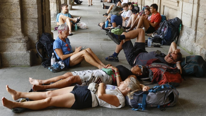 Un grupo de peregrinos descansa en los bajos del Palacio de Raxoy, en la plaza del Obradoiro, para escapar del calor, este jueves en Compostela.