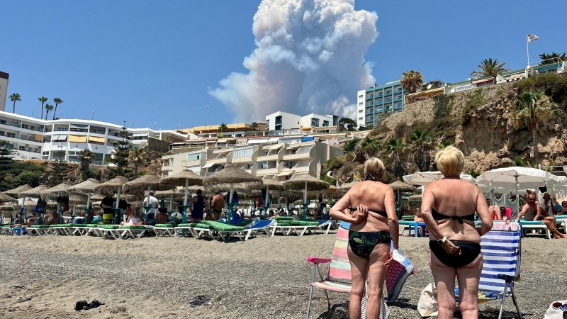 La gente mira las columnas de humo causadas por un incendio forestal en Málaga, visto desde la Playa del Bajondillo en Torremolinos, España, el 15 de julio de 2022.