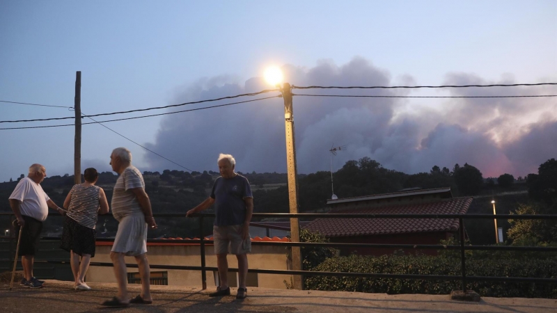 Varios vecinos observan la columna de humo del incendio forestal declarado en Monsagro, desde la localidad salmantina de Serradilla del Arroyo, en la madrugada de este viernes.