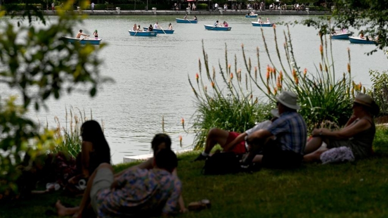 La gente se sienta a la sombra de los árboles mientras otros reman en botes en el Parque del Retiro en el centro de Madrid en la ola de calor de junio de 2022.