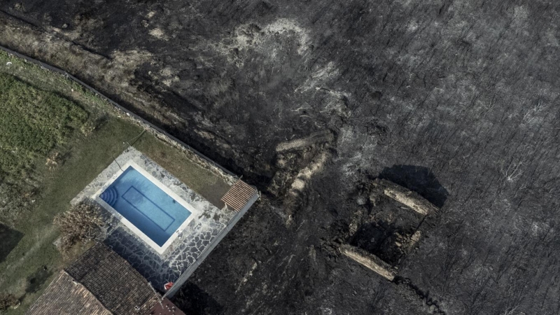 Fotografía tomada con un dron de una piscina y una construcción rodeadas por la superficie calcinada en el pueblo de San Cibrao, Oímbra, Ourense.