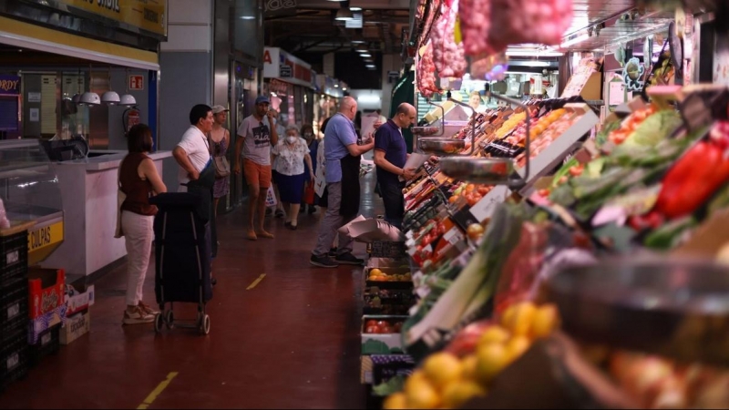 Varias personas hacen cola para hacer la compra en una frutería del Mercado de la Cebada, en Madrid.