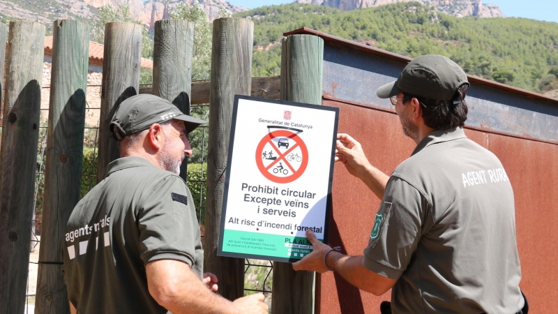 Dos Agents Rurals col·loquen un cartell informatiu a l'accés al Parc Natural de la Serra de Montsant des de la Cartoixa d'Escaladei.