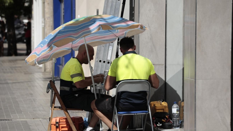 Dos operarios de telefonía se protegen con una sombrilla del intenso sol y calor en Valencia.