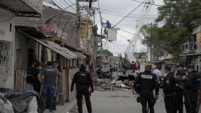 Miembros de las fuerzas de seguridad vigilan mientras los electricistas reparan cables de energía pública cerca del área de una explosión que dejó heridos y otros muertos al destruir varias casas y vehículos en el sur de Guayaquil, Ecuador.