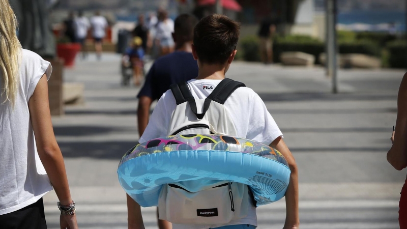 Un niño va camino de la playa del Postiguet de Alicante, hoy, último día de Agosto, con un flotador y la mochila del colegio