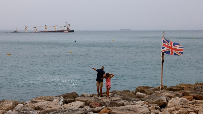 Un hombre y una niña observan desde la orilla, junto a una bandera británica, al granelero OS35, medio hundido frente a Gibraltar. REUTERS/Jon Nazca