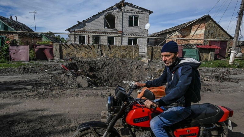 Un hombre pasa en motocicleta por casas dañadas y un cráter en el suelo en Siversk, región de Donetsk, a 20 de septiembre de 2022.