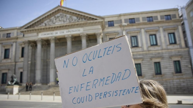 03/10/2022. Una mujer sujeta una pancarta en la que se lee: 'No ocultéis la enfermedad covid persistente' durante una sentada pacífica en Madrid, frente a las Cortes, a 18 de junio de 2022, en Madrid