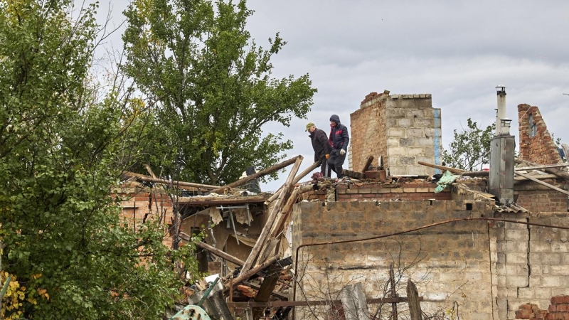 Ciudadanos limpian los escombros de un edificio dañado por los bombardeos en la aldea de Ruski Tyshky del área de Kharkiv.