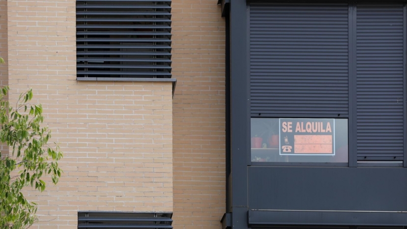 En la fachada de un edificio se ve un cartel de 'Se Alquila' bajo la persiana de uno de los pisos.
