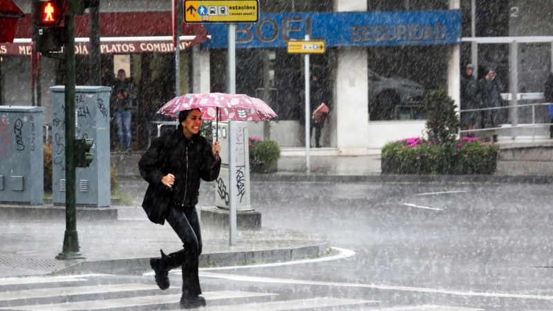 Una mujer pasa esta mañana por una calle de Compostela, enfrentándose a fuertes lluvias y a un intenso viento de una profunda borrasca procedente del Atlántico.