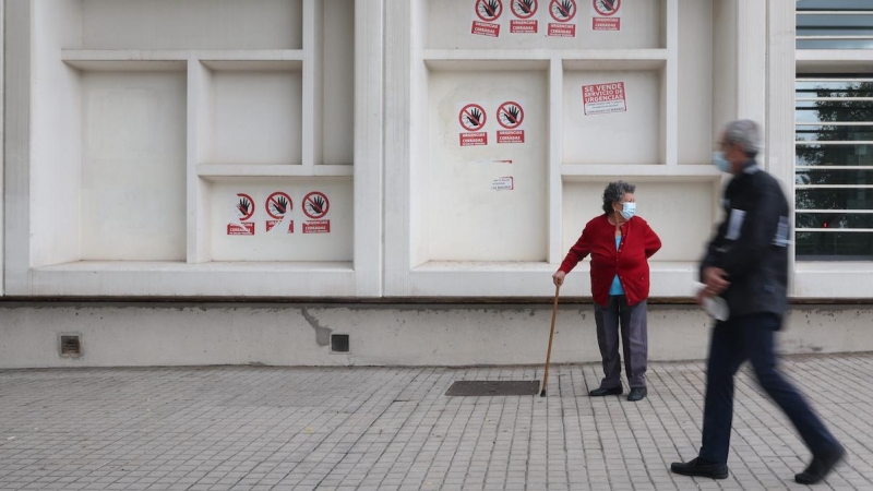 Dos personas mayores con mascarilla delante del Centro de Salud Pavones, donde hay carteles de protesta que rezan 'Urgencias Cerradas, tu salud vendida', a 21 de octubre de 2022, en Madrid.