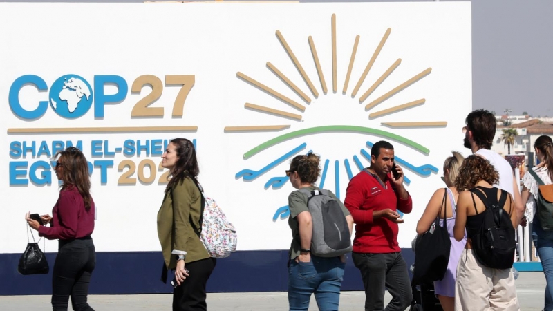 Varias personas caminan junto al cartel de la COP27 en Sharm El Sheikh, Egipto.