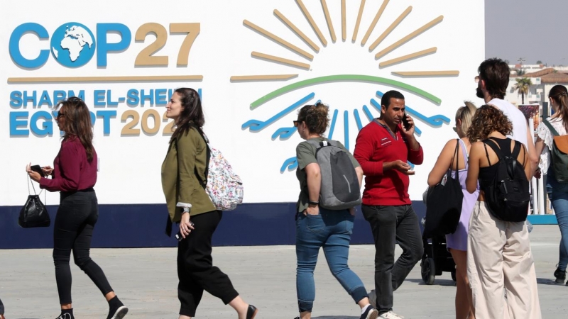 Varias personas caminan junto al cartel de la COP27 en Sharm El Sheikh, Egipto.