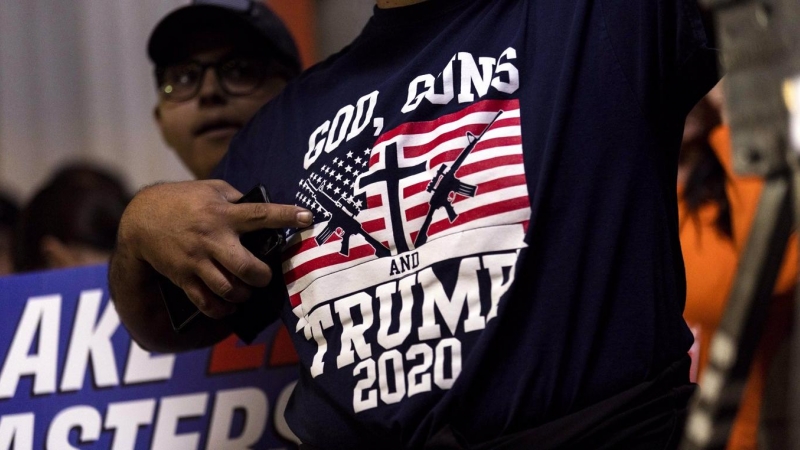 Un simpatizante republicano señala a su camiseta que dice 'Dios, armas y Trump 2020', durante un mitin  en Schnepf Farms en Queen Creek, Arizona (EEUU). EFE/Etienne Laurent