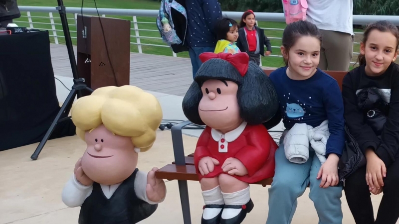 Dues nenes assegudes al costat de la nova escultura de Mafalda, a Santa Coloma de Gramenet.