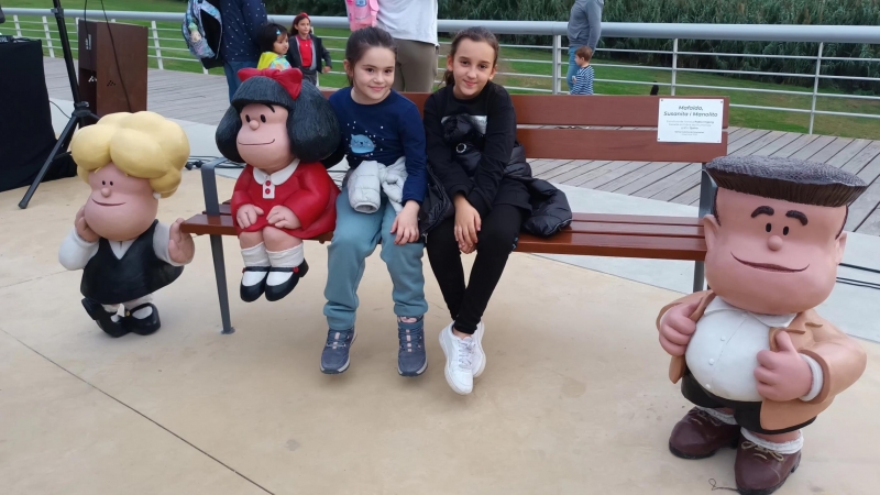 Dues nenes assegudes al costat de la nova escultura de Mafalda, a Santa Coloma de Gramenet.