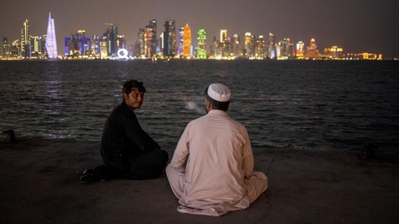 13/11/2022 Dos hombres charlan a la orilla del río con vistas al 'skyline' de Doha (Qatar)