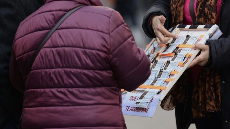 Una mujer compra un décimo de lotería a una vendedora ambulante.