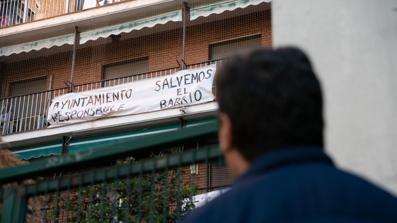 Ángel, vecino de Puerta del Ángel, mira la pancarta de un vecino con el lema 'Salvemos el barrio'.