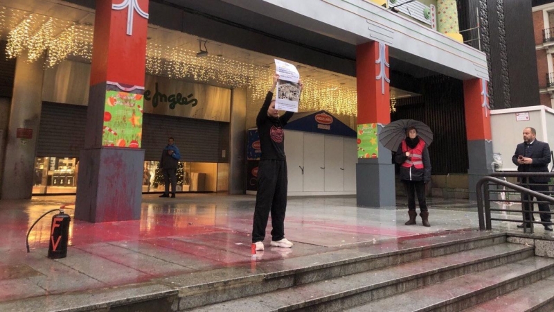 Una activista sostiene una pancarta tras rociar con pintura parte del escenario navideño infantil de Cortylandia.