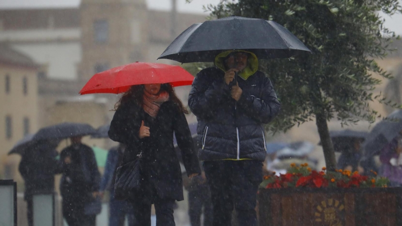 Unas personas se protegen con paraguas de la lluvia mientras caminan por el puente romano de Córdoba en una jornada en la que la ciudad se encuentra en aviso amarillo por lluvias.