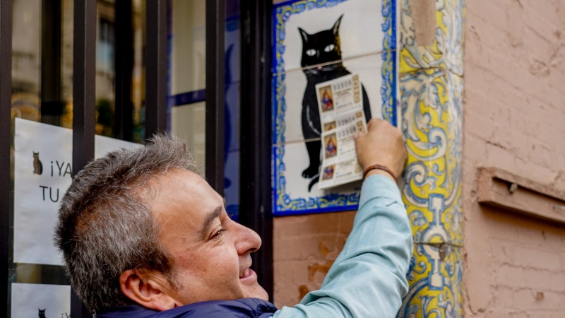Una persona pone el décimo recién comprado en el azulejo que representa a el gato negro en la administración de loterías ‘El Gato Negro’ en Sevilla- 07/12/2022