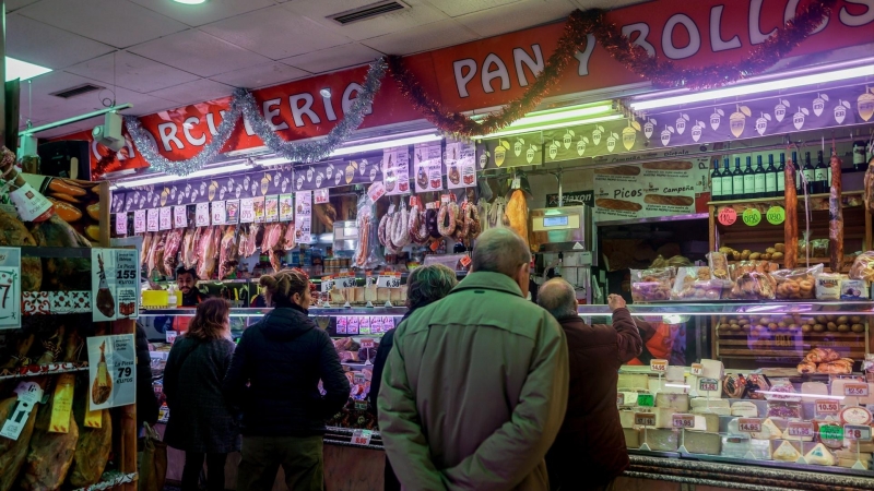 Varias personas esperan a ser atendidas en un puesto de productos alimentarios.