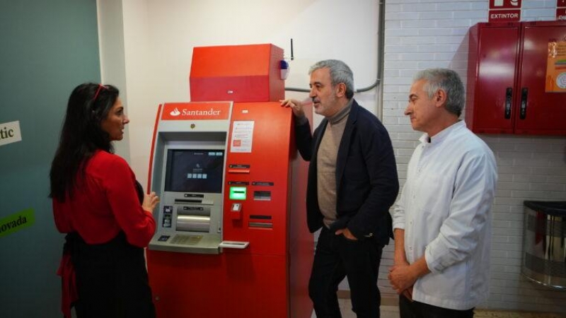 El tinent d'alcaldia d'Economia de Barcelona, Jaume Collboni, amb el president del Mercat del Besòs, Joaquim Tomás, i la propietària d'una parada de llegums, Lourdes Mulero, amb el caixer bancari instal·lat en aquest equipament.