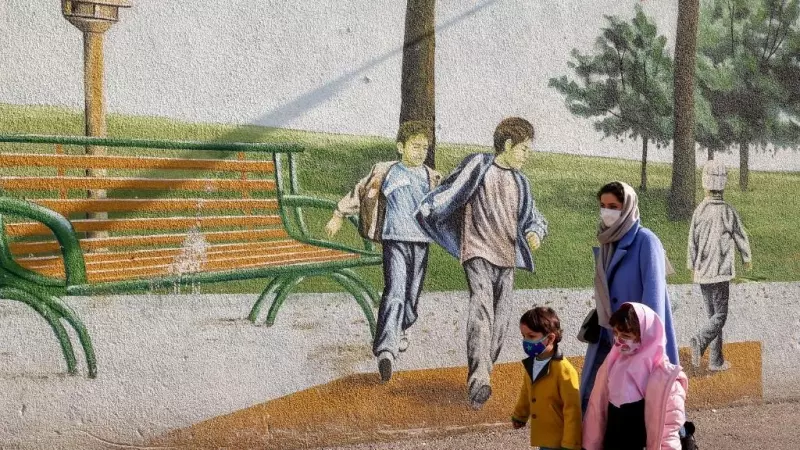 Una mujer pasea junto a sus hijos frente a un mural infantil en Teherán.
