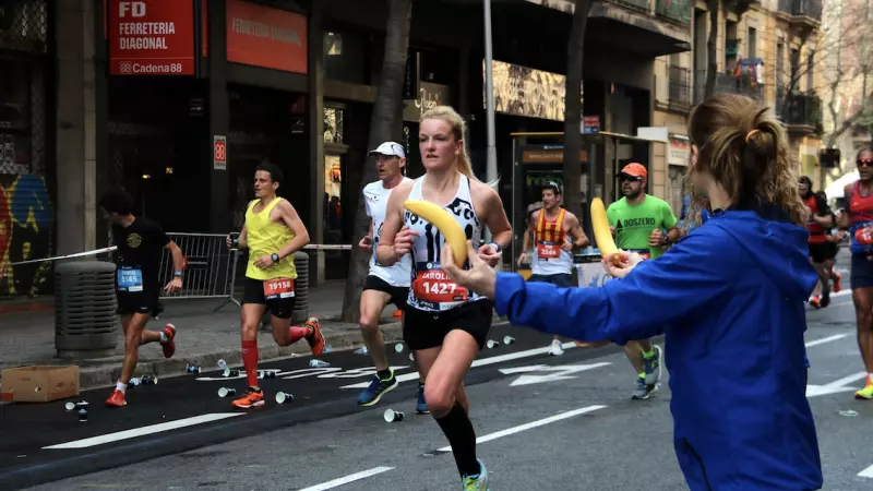 17-3-2023 Una voluntària ofereix un plàtan a una participant mentre corre a la Marató de Barcelona