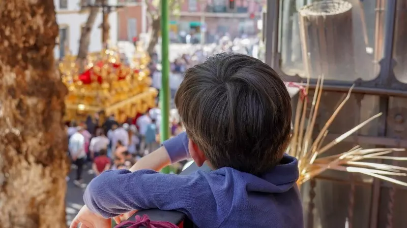 Un niño viendo desde un balcón el cortejo de la Hermandad de la Sed, en Sevilla. E.P./Eduardo Briones