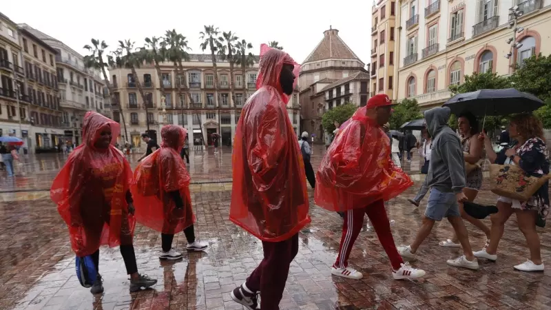 Un grupo de personas se tapan de la lluvia y el viento en una calle de Málaga, a 18 de mayo de 2023.