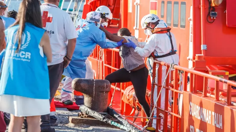 Agentes de salvamento marítimo ayudan a una mujer migrante a desembarcar de la guardamar Talía en Arguineguín.