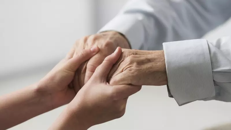 Una enfermera sostiene las manos de una persona mayor