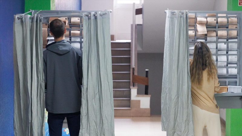 Dos personas ejercen su derecho a voto en una cabina en un colegio electoral, a 28 de mayo de 2023, en Madrid
