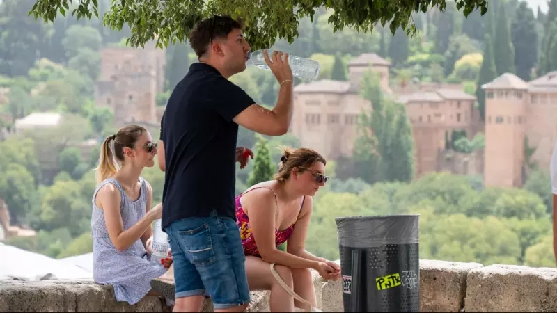 Unos turistas descansan a la sombra y beben agua con la imagen de la Alhambra de fondo, a 11 de julio de 2023