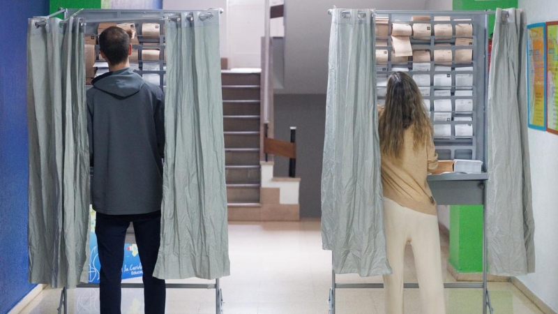 Dos personas ejercen su derecho a voto en una cabina en un colegio electoral, a 28 de mayo de 2023, en Madrid