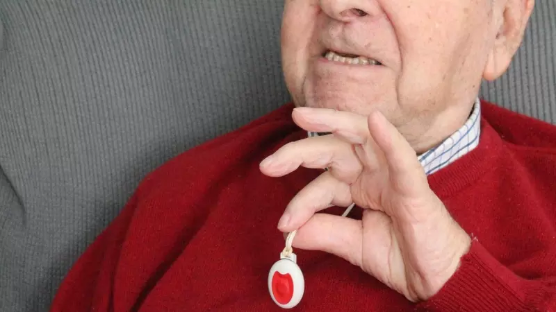 Una persona mayor muestra el botón de la teleasistencia.