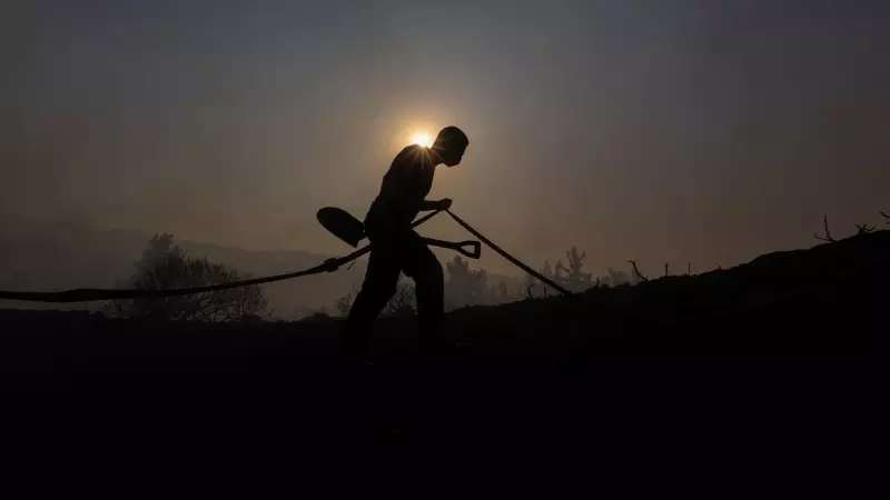 Se recorta la silueta de un voluntario mientras lleva una pala y una manguera mientras un incendio forestal arde cerca del pueblo de Asklipieio, en la isla de Rodas, Grecia , el 24 de julio de 2023.