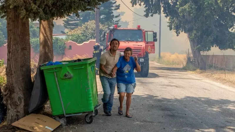 Un hombre ayuda a una mujer a evacuar, mientras un incendio forestal arde cerca del pueblo de Kiotari, en la isla de Rodas, Grecia.