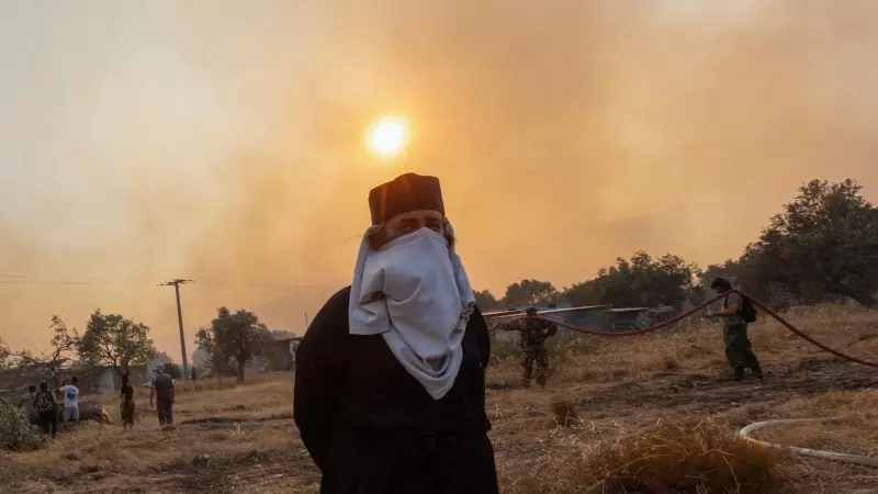 Un sacerdote ortodoxo griego se cubre la cara para protegerse del humo mientras los bomberos, voluntarios y policías se preparan para hacer frente a un incendio forestal que se acerca al pueblo de Masari, en la isla de Rodas, Grecia