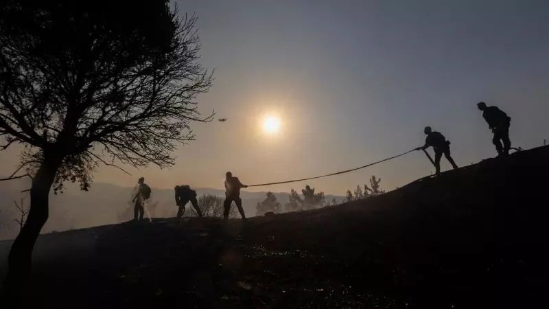 Bomberos, voluntarios y policías se perfilan mientras llevan una manguera, mientras un incendio forestal arde cerca del pueblo de Asklipieio, en la isla de Rodas, Grecia , el 24 de julio de 2023.