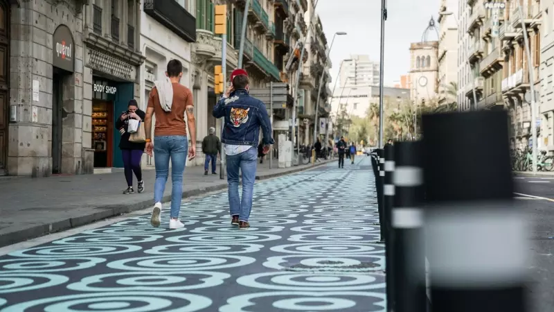 Pla general de dos homes caminant pel carrer Pelai, amb l'espai per a vianants pintat amb panots blaus, en una imatge d'arxiu