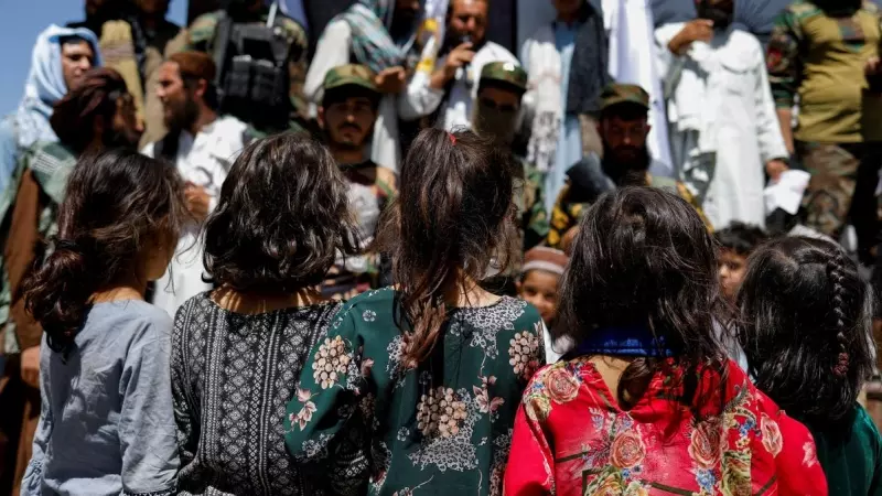 Niñas afganas observan a simpatizantes talibanes en el segundo aniversario de la caída de Kabul en una calle cerca de la embajada de EEUU en Kabul