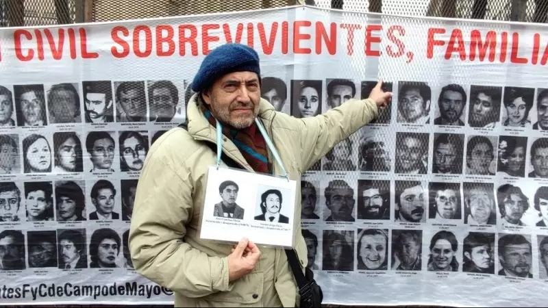 Un hombre posa junto a un cartel con fotografías de las víctimas y desaparecidos de la dictadura argentina.