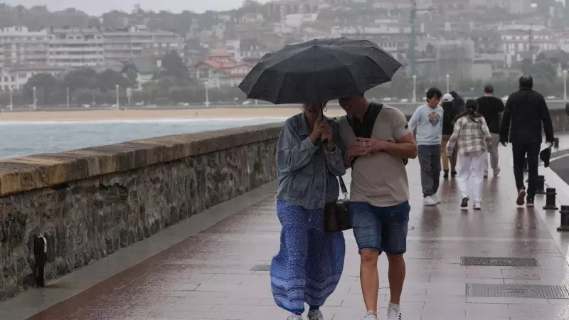 Dos personas se protegen de la lluvia con un paraguas en la playa de Ondarreta, a 14 de octubre de 2023, en San Sebastián