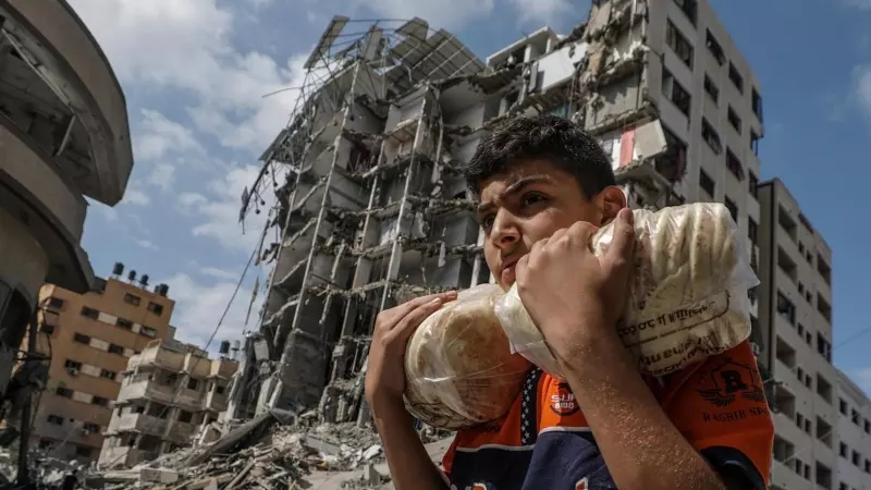 16/10/23 Un joven palestino porta dos bolsas de pan este lunes 16 de octubre frente a un edificio bombardeado en el barrio de Al Remal, en la ciudad de Gaza.